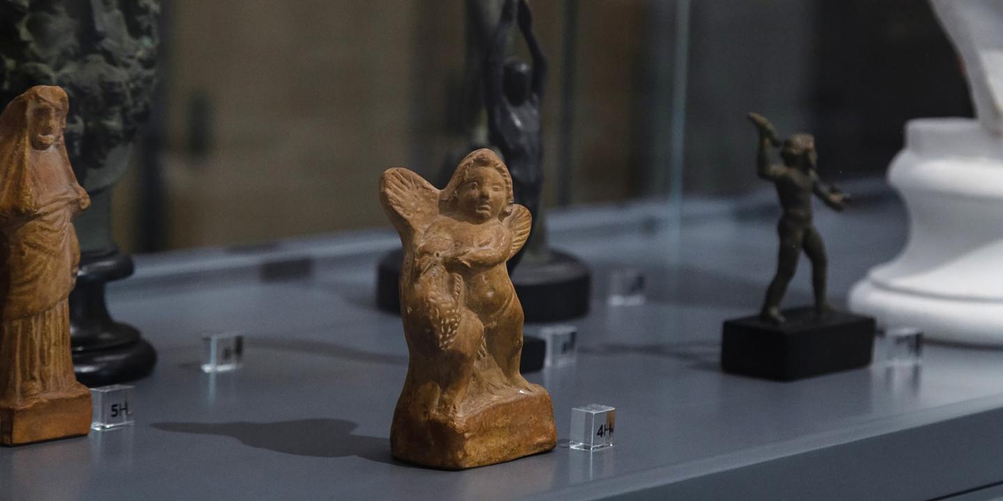 Vitrīnā izstādītas nelielas skulptūras, tostarp spārnota figūra un citas cilvēkveidīgas statuetes uz pamatnēm.
