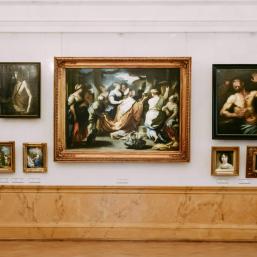 Skats uz muzeja izstāžu zāli ar klasiskās mākslas gleznām greznos rāmjos pie sienas.