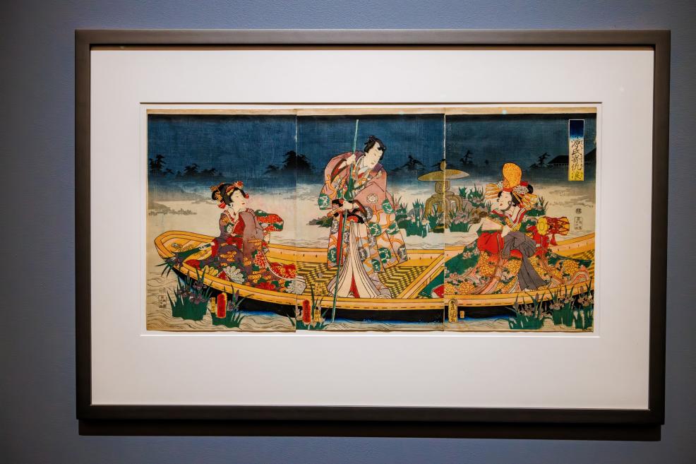 A framed Japanese color woodblock print depicting three figures in a boat set against a nighttime scene.