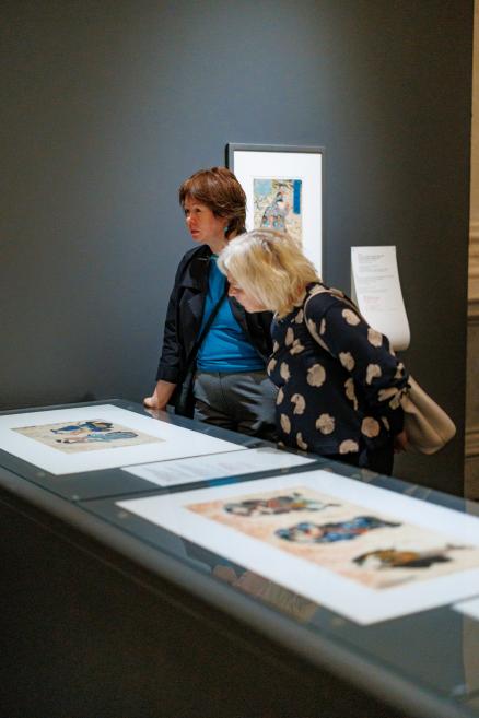 Two visitors examining Japanese prints displayed in a glass-topped exhibition table in the museum gallery.