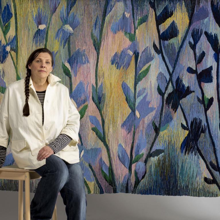 Tekstilmākslinieces Ivetas Vecenānes portrets ar gobelēnu &ldquo;Cigoriņi&rdquo; (2019). 2025. Foto: Didzis Grodzs