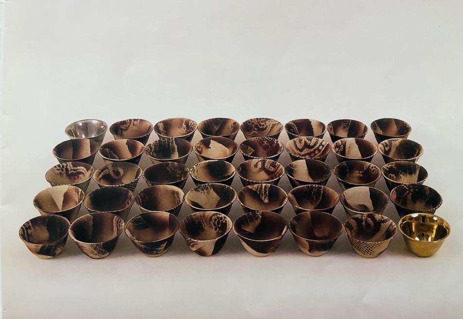 Rows of small ceramic bowls in brown tones with one striking golden bowl in the foreground.