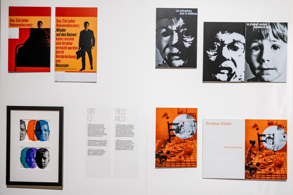 Tuvplāns ar izstādes plakātiem dažādās valodās, tostarp vācu un franču.