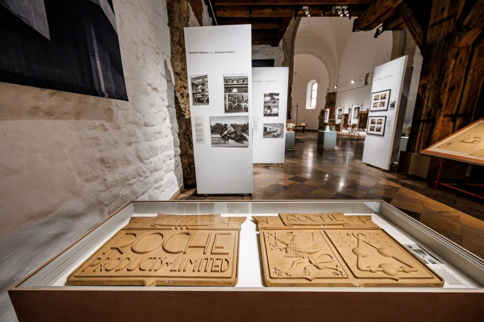 Stikla vitrīnā izstādītas dekoratīvas plāksnes ar Roche uzrakstu un simboliem.