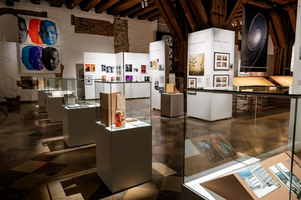 Plašs izstādes zāles skats ar stendiem, fotogrāfijām un vitrīnām par Roche arhitektūru un dizainu.