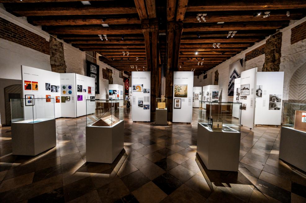 Izstādes zālē redzams liels melnbalts baneris un izvietoti arhitektūras rasējumi par Roche ēkām.