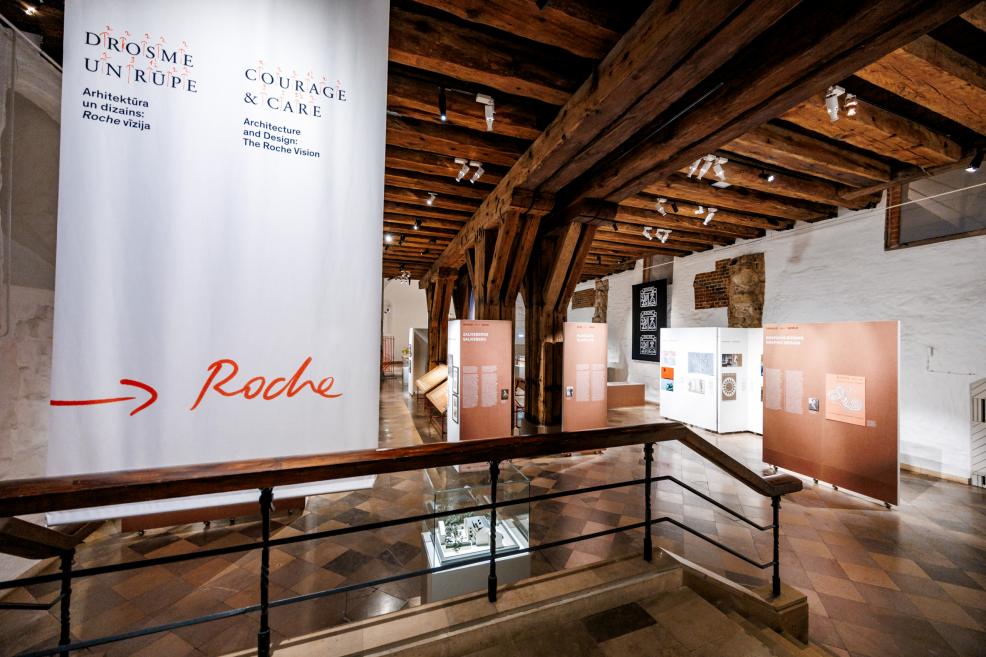 Izstādes skats ar lielu auduma baneri “Courage &amp; Care. Roche Vision”.