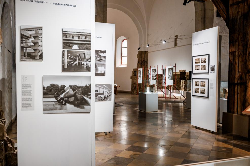 Izstādes stends ar melnbaltām fotogrāfijām un arhitektūras dokumentiem par Roche ēkām.
