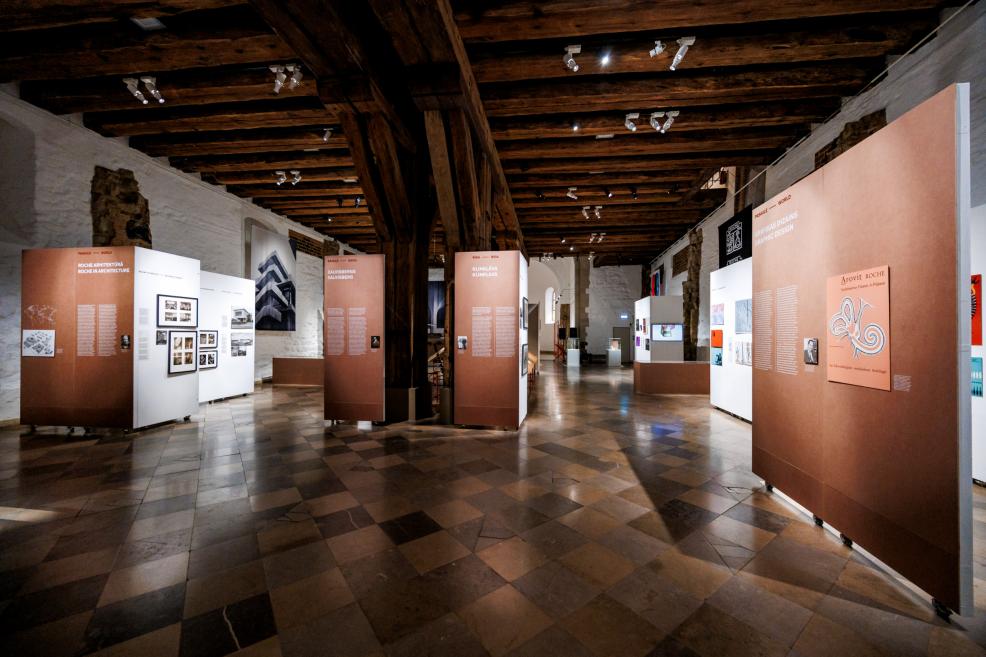 Izstādes telpa ar brūniem un baltiem stendiem, kas stāsta par Roche arhitektūru un dizainu.