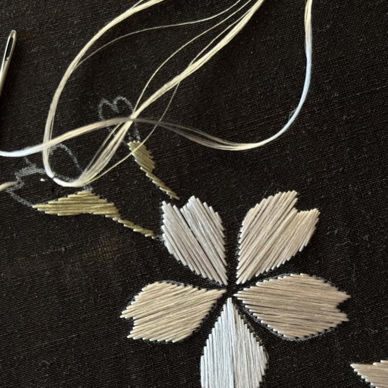 Tekstila izšuvuma detaļa ar adatu un diegu uz tumša auduma.