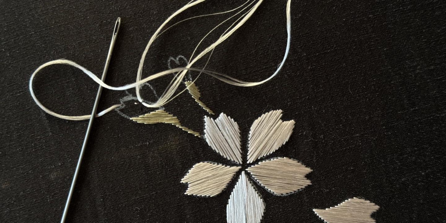 Tekstila izšuvuma detaļa ar adatu un diegu uz tumša auduma.