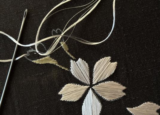 Tekstila izšuvuma detaļa ar adatu un diegu uz tumša auduma.