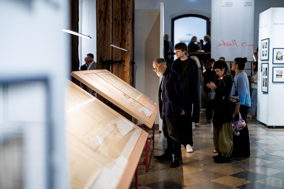 Four men at the exhibition observe a display case near the Roche emblem.