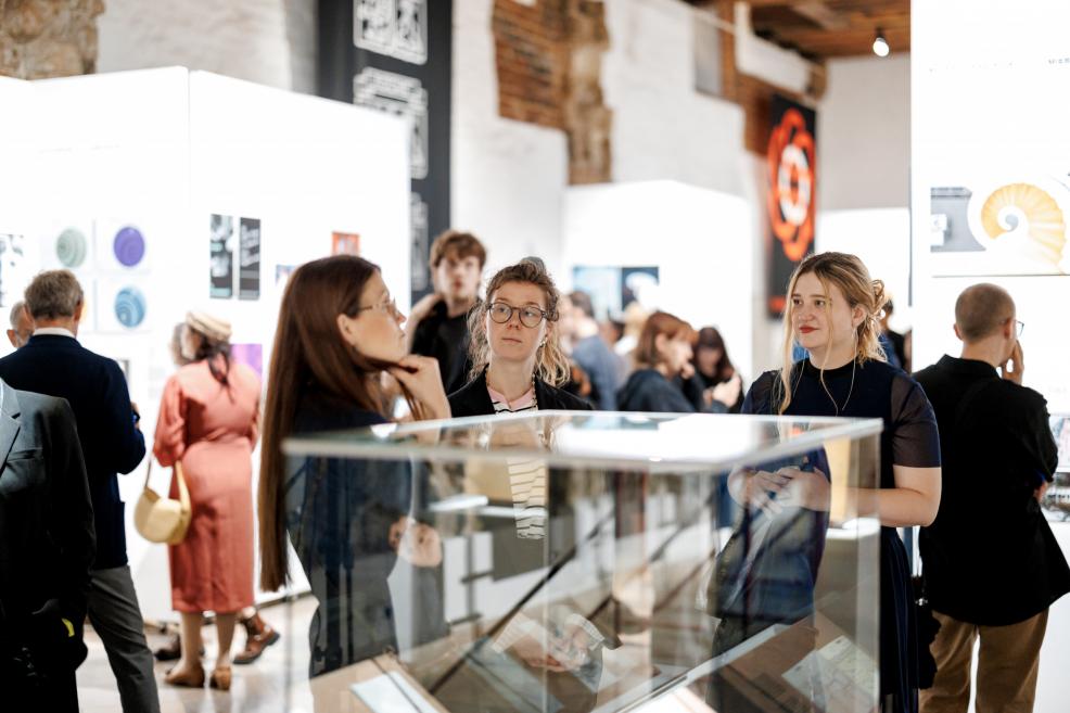 A woman in orange stripes observes black-and-white architectural photographs at the exhibition.