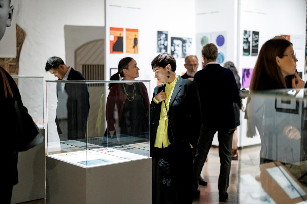 Visitors at a museum exhibition view exhibits displayed in glass showcases.