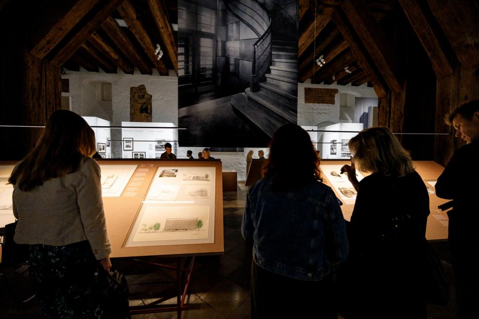 Visitors stand by large tables viewing architectural drawings and models.