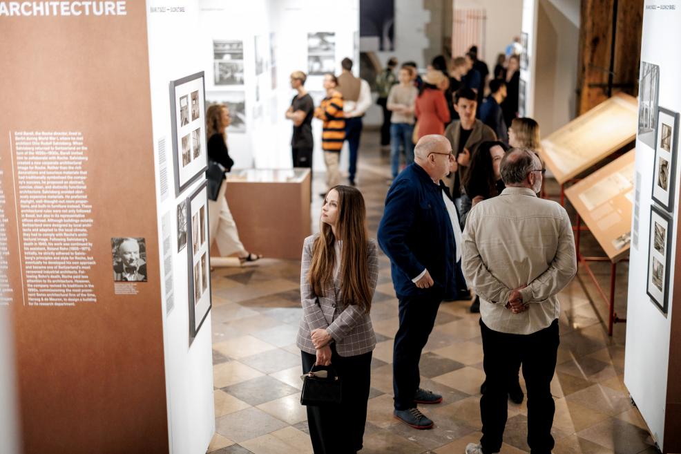 A woman reads exhibition texts and looks at photographs on the wall.