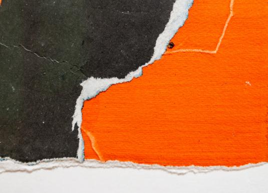 Tuvplāna fragments ar plēstas faktūras papīra gabaliem spilgti oranžā un tumši pelēkā tonī, pārklājoties uz balta fona.