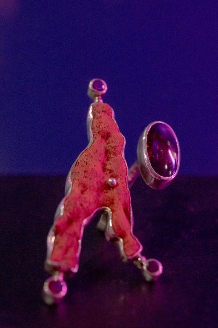 A close-up of an abstract red-pink metal or resin sculpture against a dark purple background.