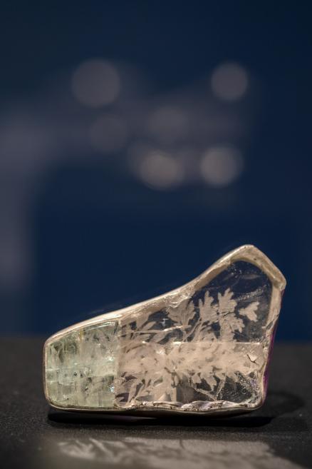 A transparent glass or crystal object with an etched plant motif is placed on a black surface against a dark background.