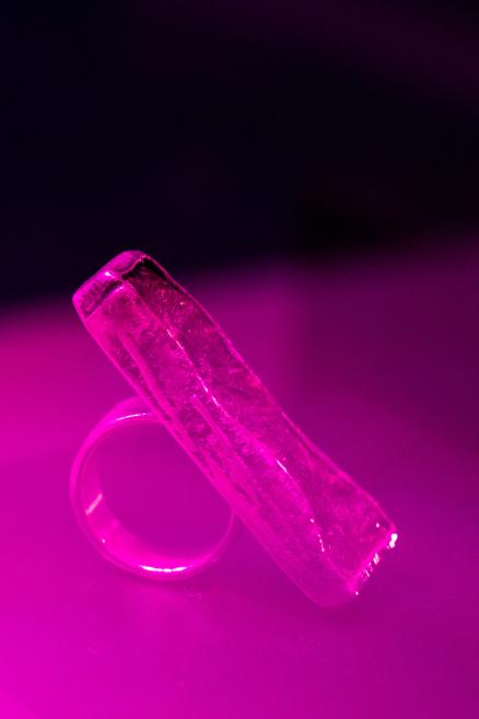 In pink lighting, a transparent crystal or glass elongated object rests on a ring-shaped base in a dark space.