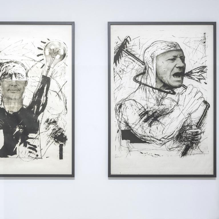 Baltā izstāžu zālē pie sienas eksponēti divi liela formāta melnbalti grafikas darbi ar ekspresīvām cilvēka figūrām, kuru priekšā kustībā izplūdis apmeklētājs aplūko darbu anotāciju.