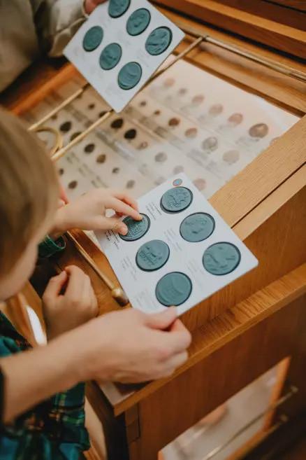 Bērni pie vitrīnas salīdzina reljefa zīmogus ar muzeja monētu kolekciju.