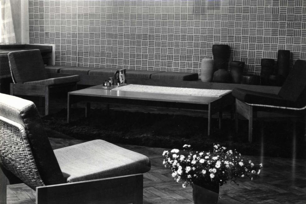 Melnbalta fotogrāfija ar modernisma stila atpūtas zonu, kurā redzami krēsli, galdiņš, paklājs un dekoratīvi priekšmeti.