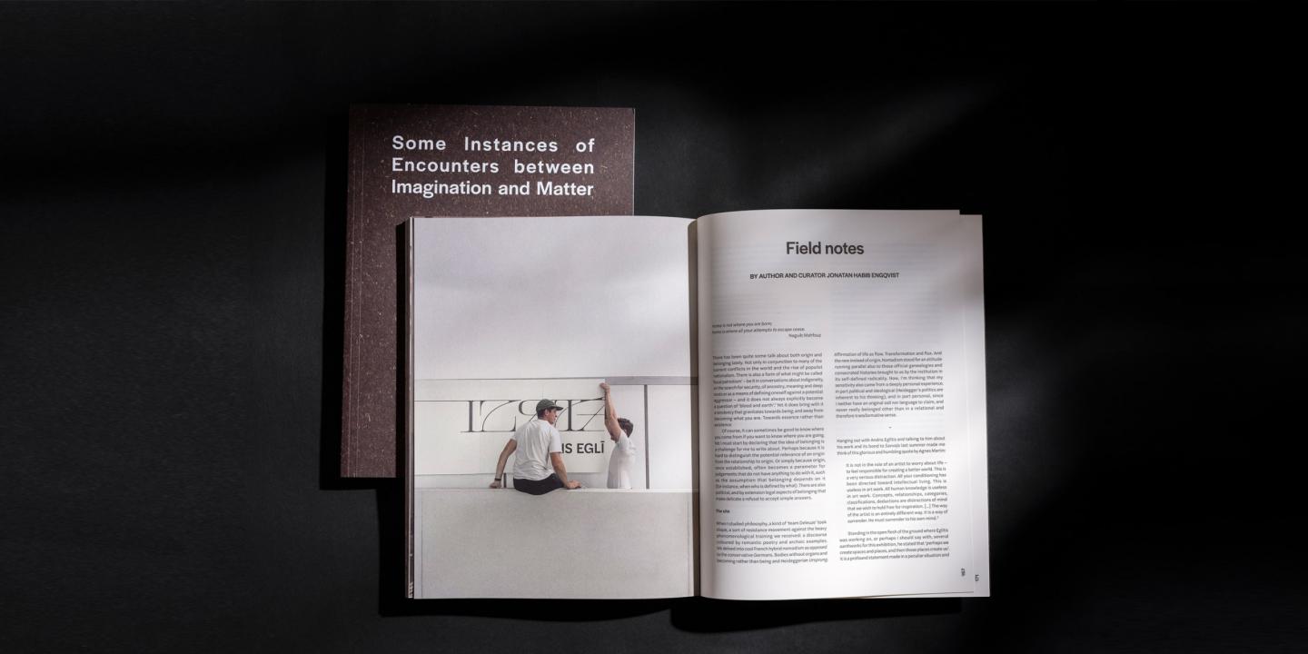 Uz melna fona novietota atvērta grāmata ar tekstu un fotogrāfiju, blakus kurai redzams tās vāks ar nosaukumu “Some Instances of Encounters between Imagination and Matter”.