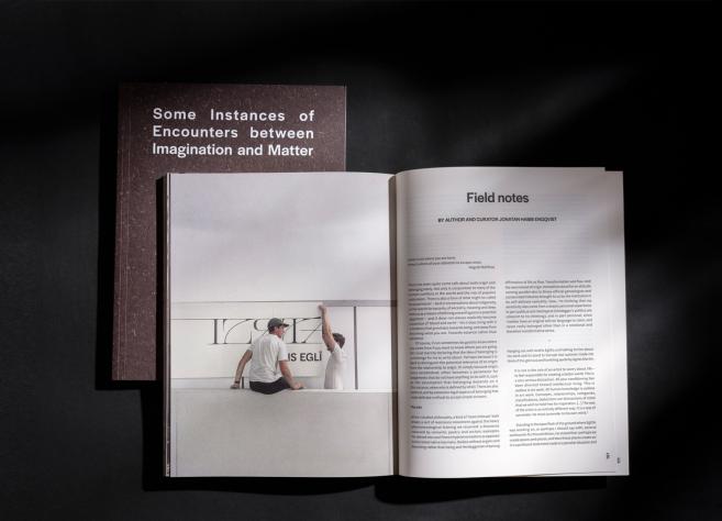 Uz melna fona novietota atvērta grāmata ar tekstu un fotogrāfiju, blakus kurai redzams tās vāks ar nosaukumu “Some Instances of Encounters between Imagination and Matter”.